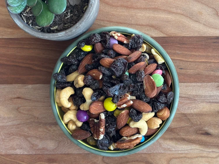 Overhead shot of a bowl of trail mix containing dried fruit, buts, and candy-coated chocolates.